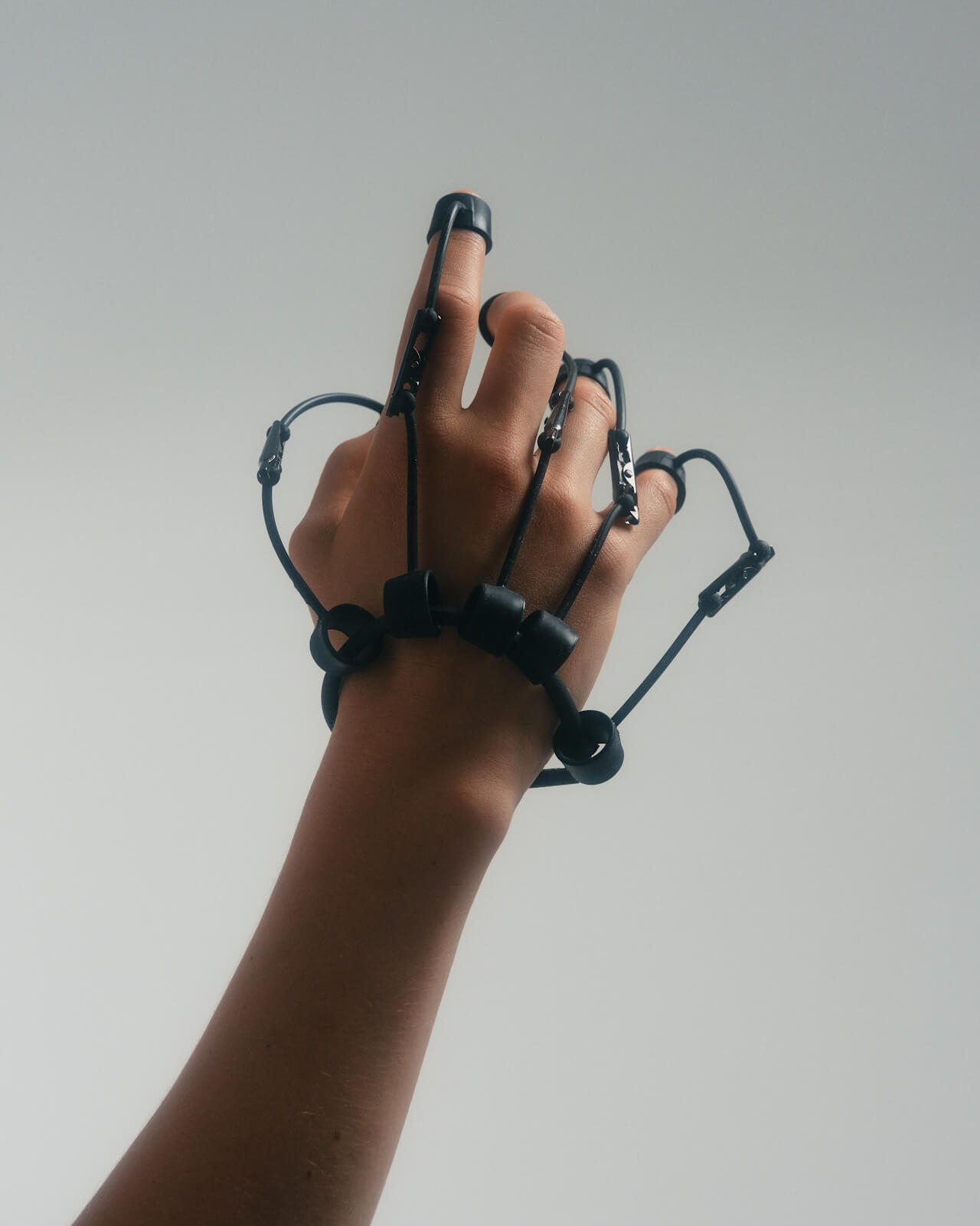 A hand is wearing a black mechanical glove with multiple loops and connectors around the fingers.