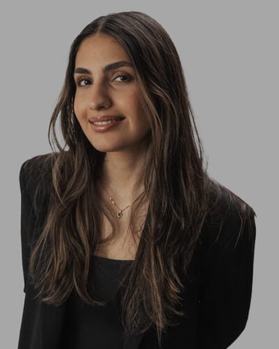 Golsa Meshkat, Designer, Takt Agency, with long brown hair, smiles at the camera. She is wearing a black shirt and blazer against a plain gray background.