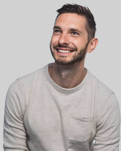 Smiling man with short brown hair and beard wearing a light gray sweater, looking upward against a gray background.