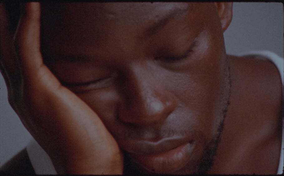 A person is resting their head on their hand with eyes closed, appearing to be in a relaxed or thoughtful state. The background is out of focus, emphasizing the serene expression on the persons face.