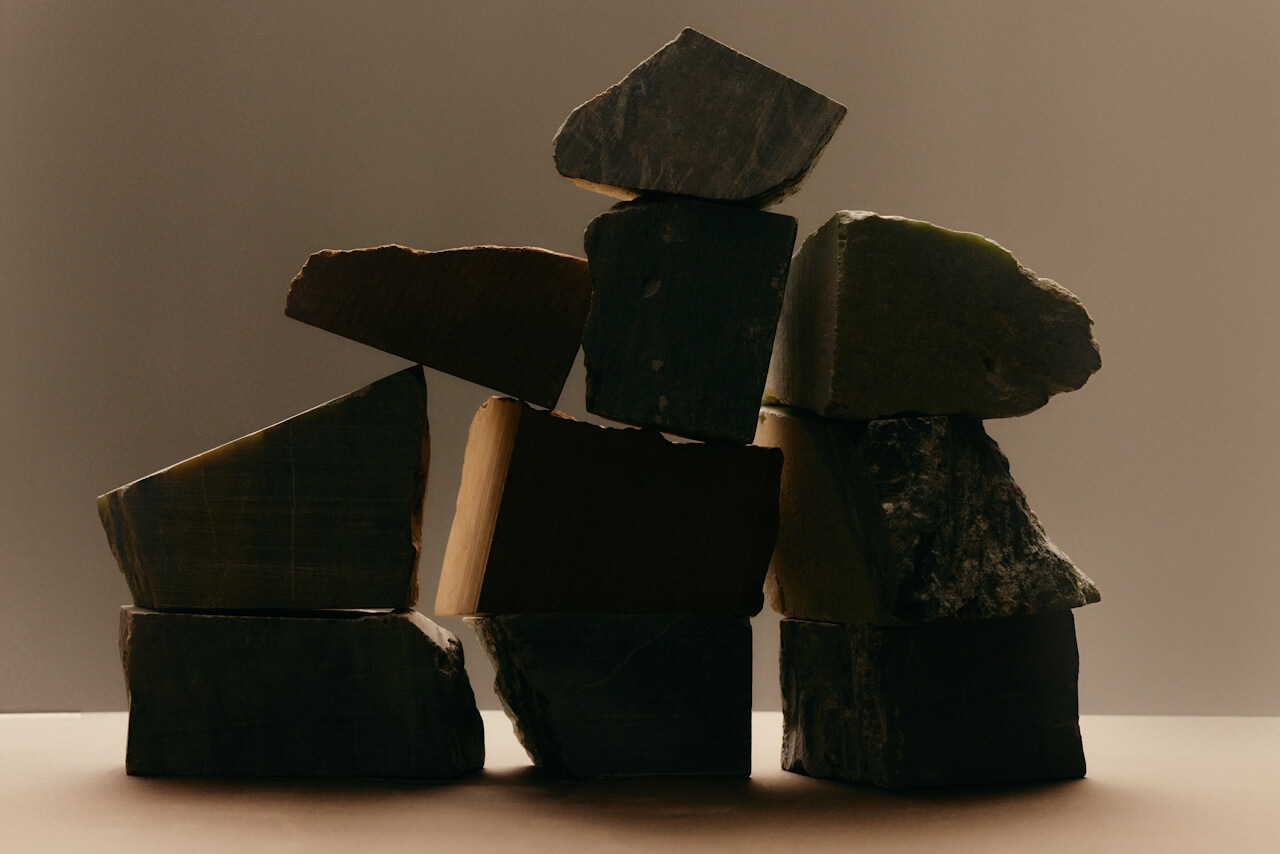 A stack of uneven, dark stone blocks balanced on each other against a plain, softly lit background.